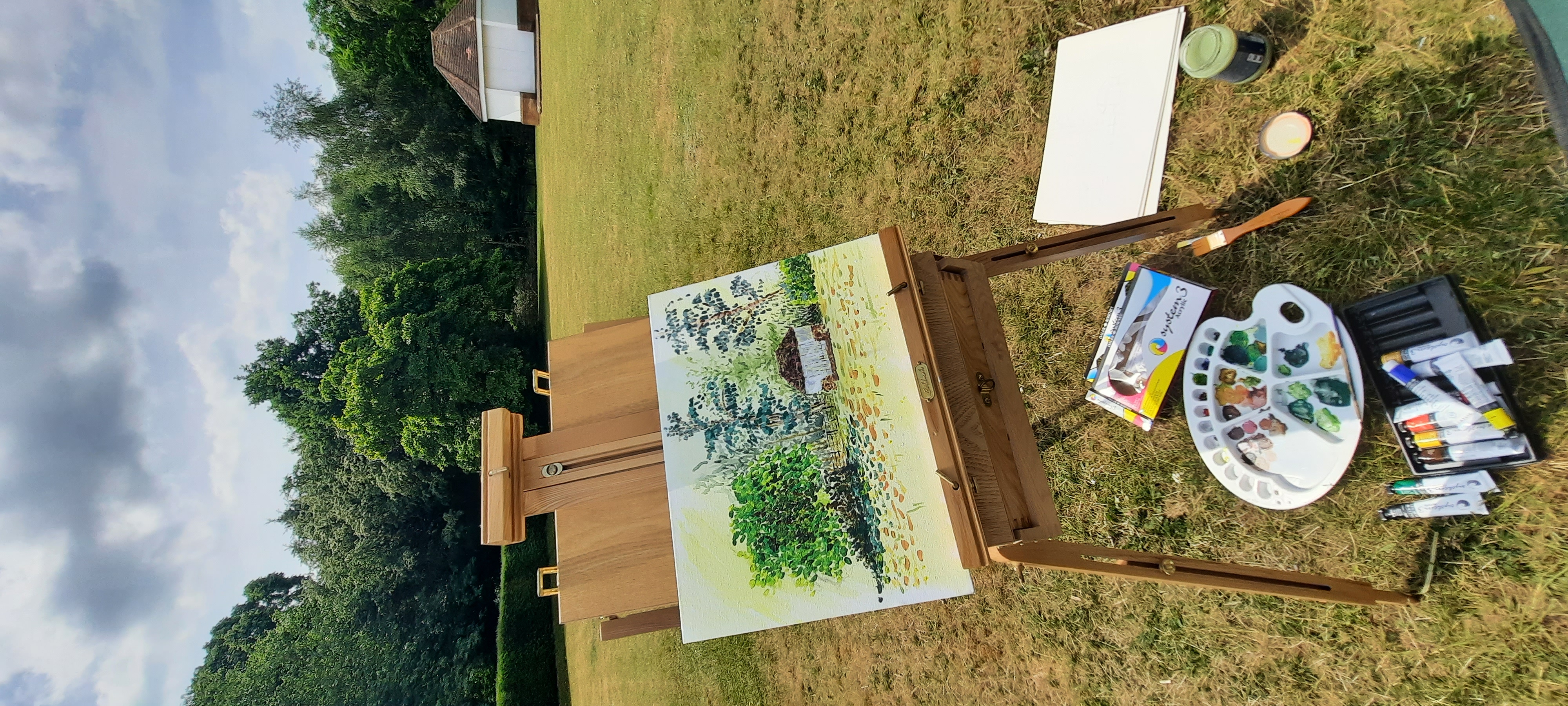 A painting on an easel of a field with a cottage
