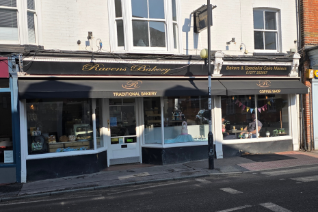 Exterior image of Ravens Bakery, a white building with large windows and black awning with gold lettering.