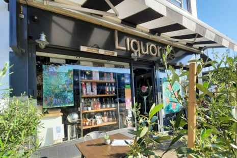 Image of the exterior of Liquorice Wine & Deli in Ingatestone. Black and white awning can be seen, along with artwork in the window, tables and chairs outside and shelves of products in the window