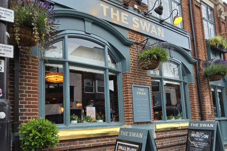 Exterior of The Swan pub in Brentwood High Street, the windows and long sign are painted green. THE SWAN is in gold lettering.