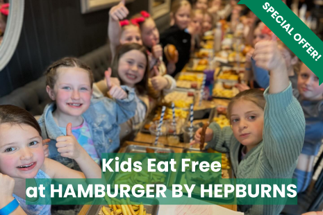 Image promoting a special offer from Hamburger by Hepburns.  An image of children around a table with text overlayed, reading 'Kids Eat Free at HAMBURGER BY HEPBURNS'.